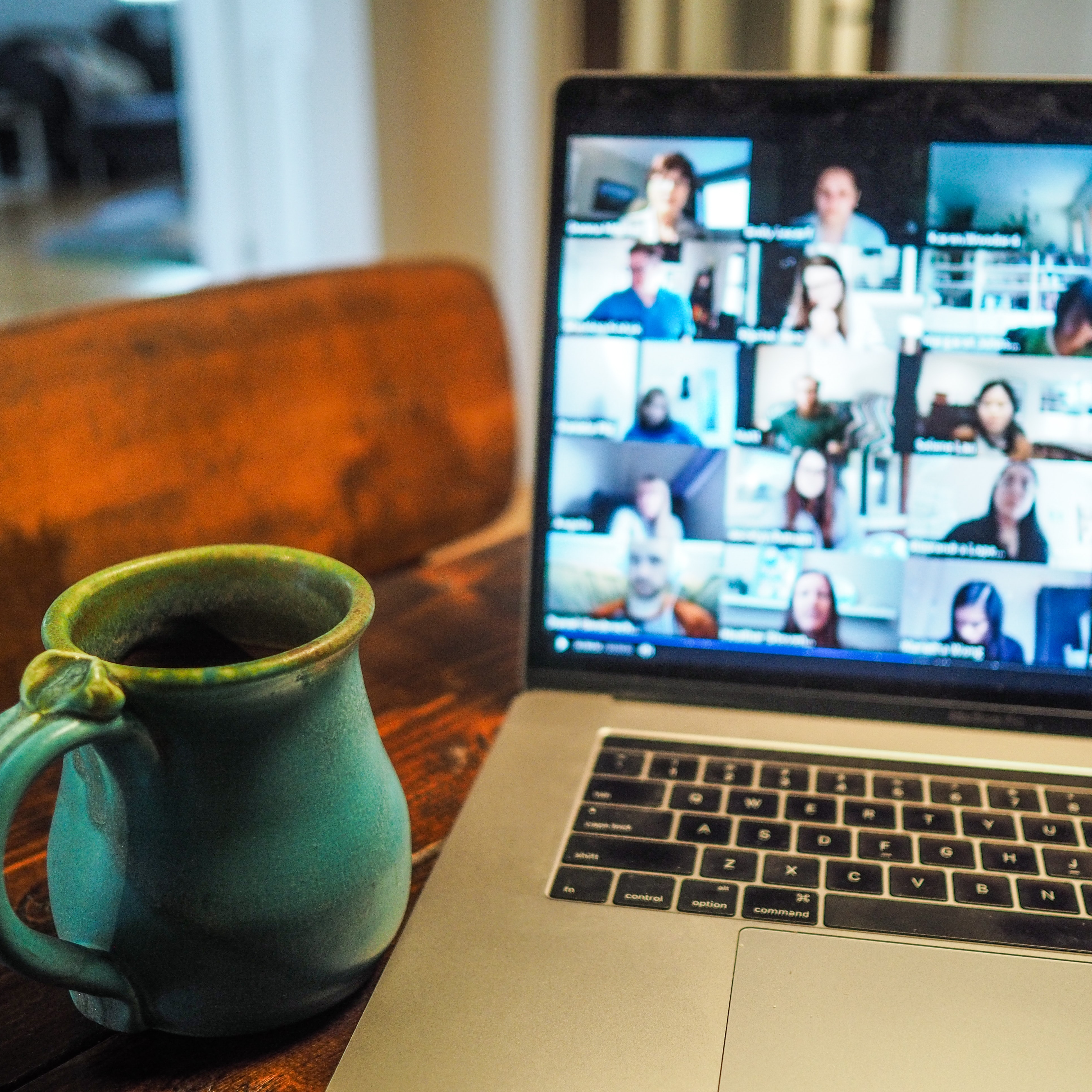 A cup of coffee next to a laptop with a Zoom meeting on the background.