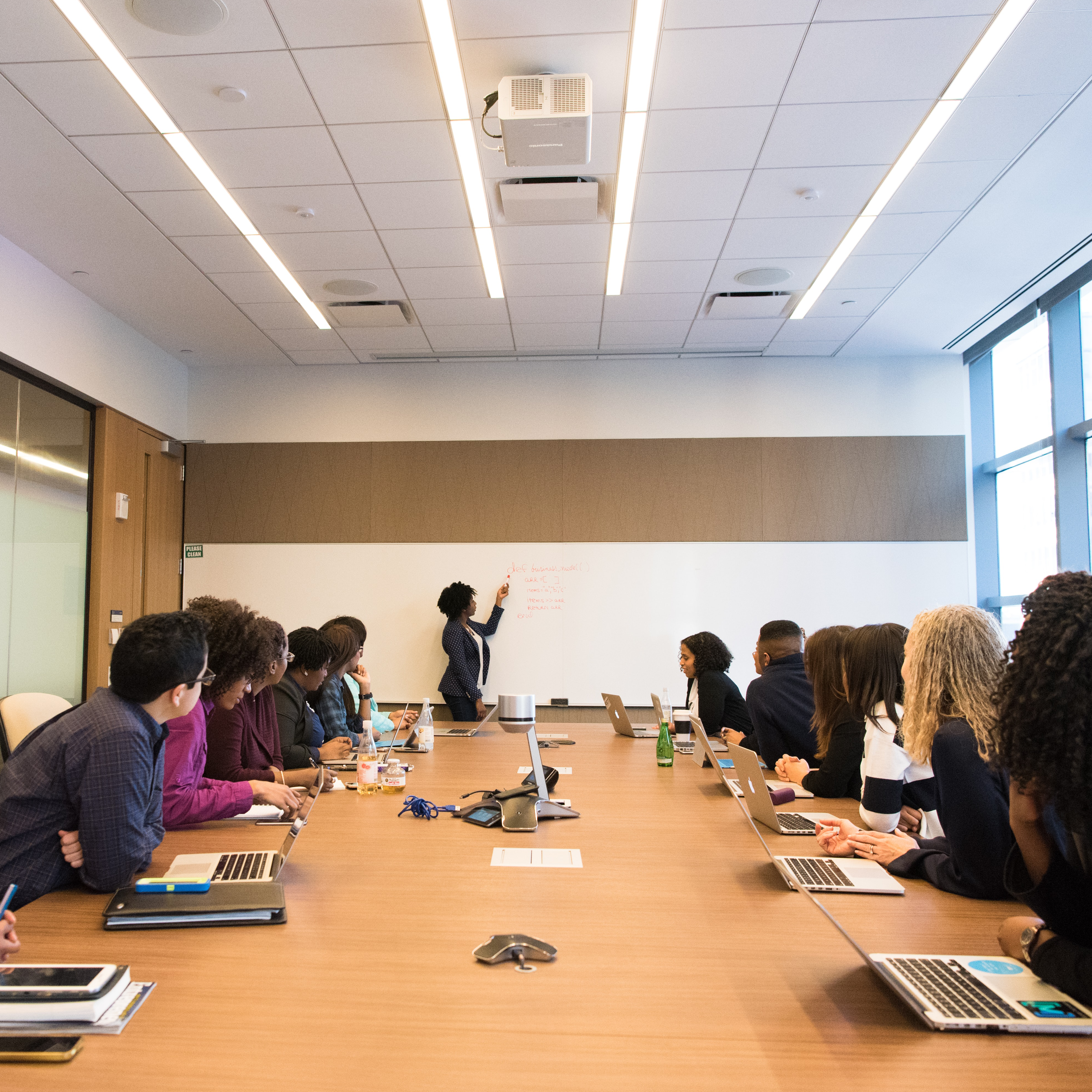 Corporate boardroom with individuals on both side of the table and one inidividual giving a presentation.